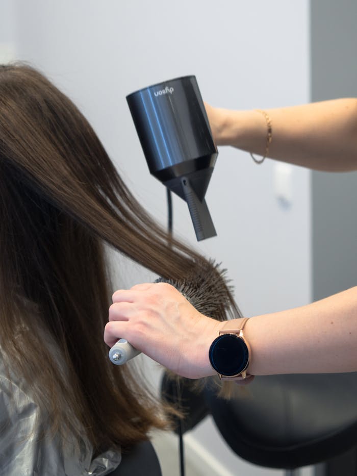 services-02 Close-up of a hairdresser using a hairdryer and brush for styling in a salon.