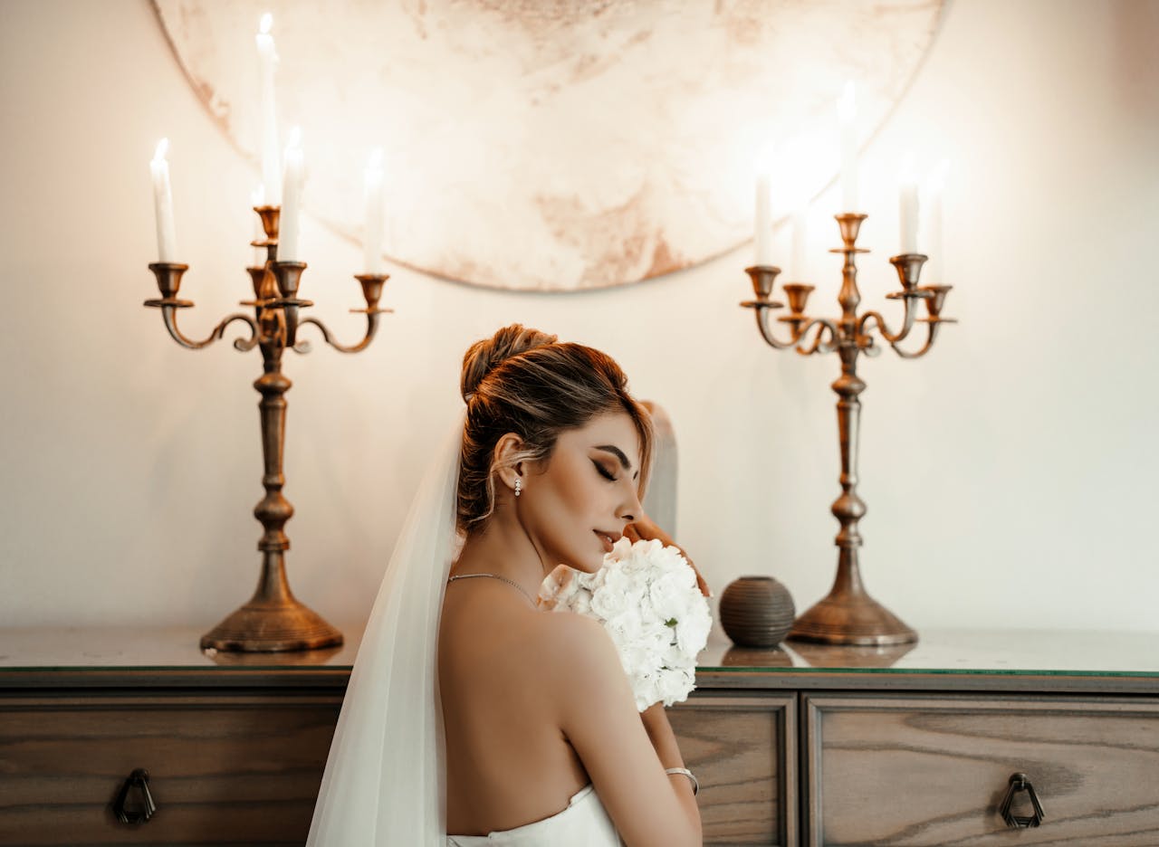 about-us A serene bride in a white gown holding a bouquet, surrounded by candles.