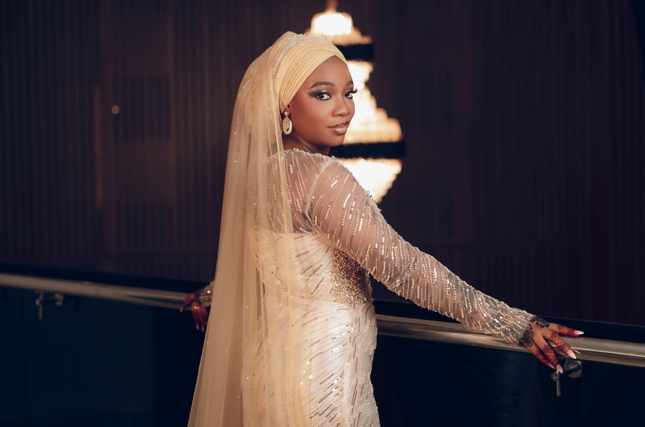 who-we-are Elegant bride in shimmering dress posing indoors with soft lighting and chandeliers.